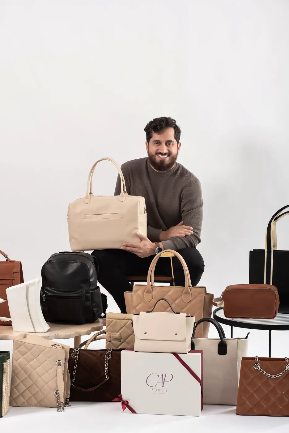 Professor Bruno segurando uma bolsa creme entre várias bolsas e mochilas