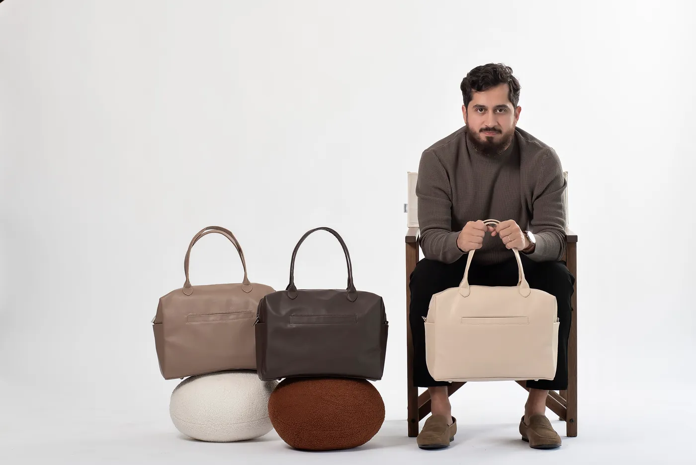 Professor Bruno sentado com três bolsas em tons neutros